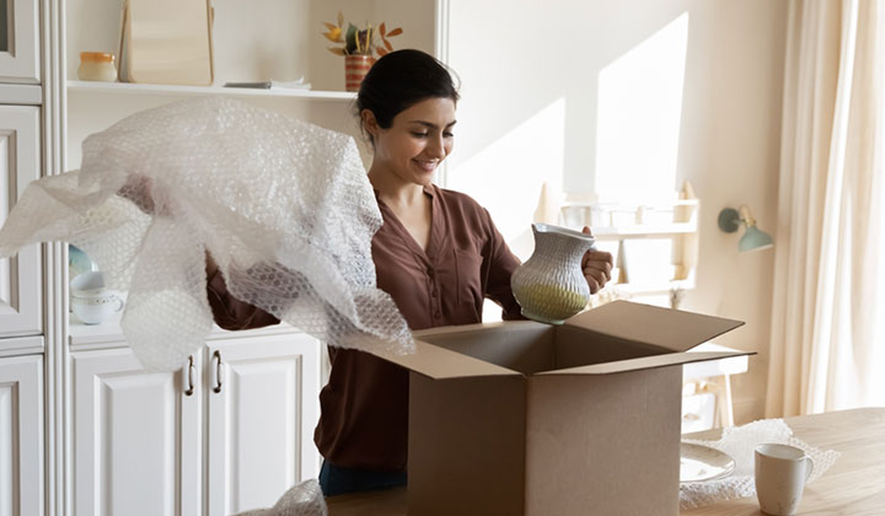 Young smiling woman unpacking a vase from a box
