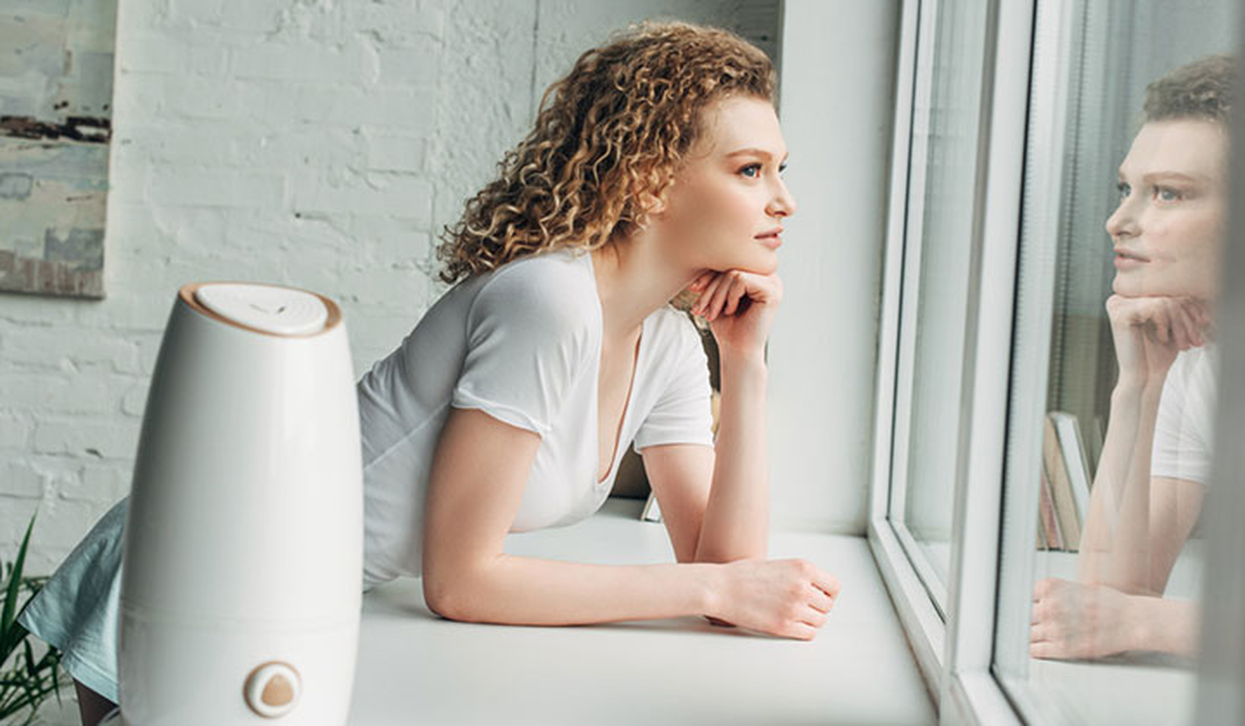 Young woman looking out window with an air purifier nearby