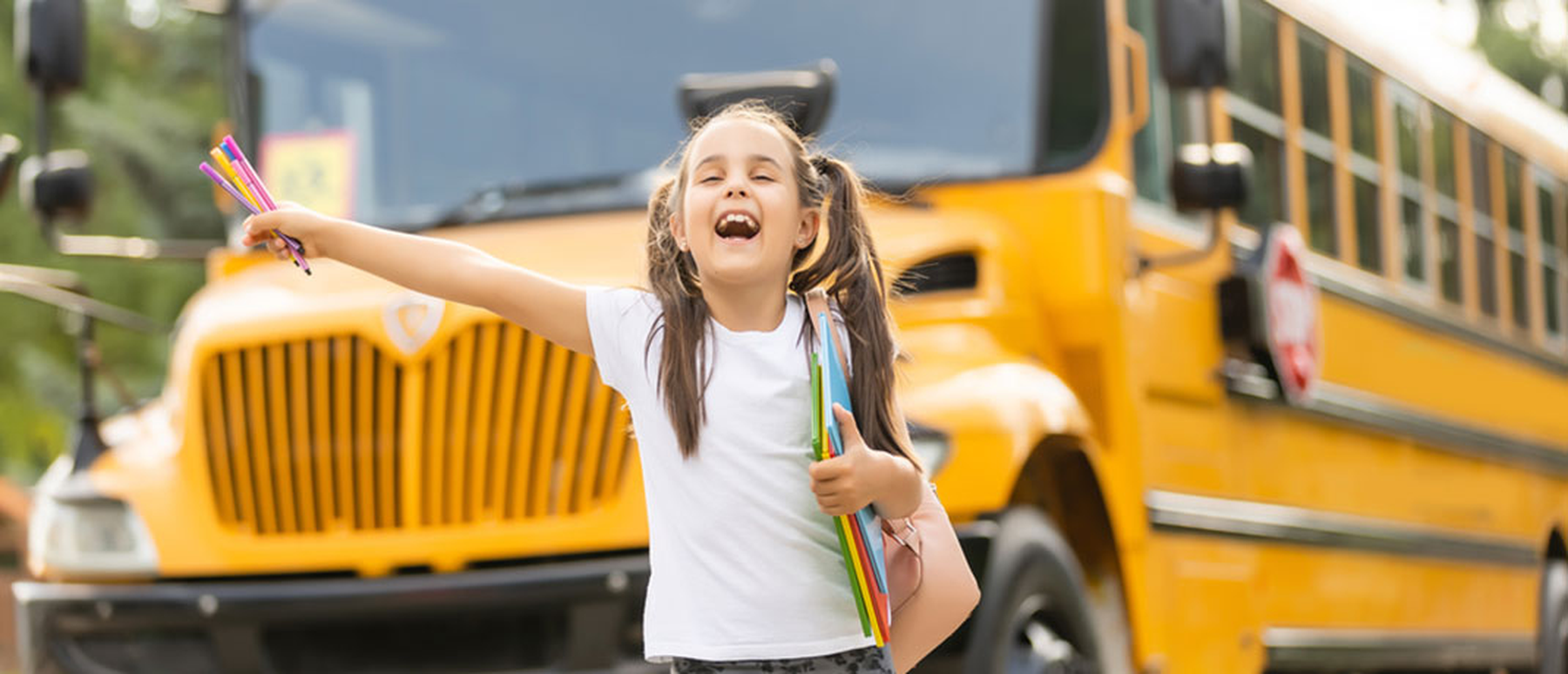 Smiling girl in front of a yellow school bus