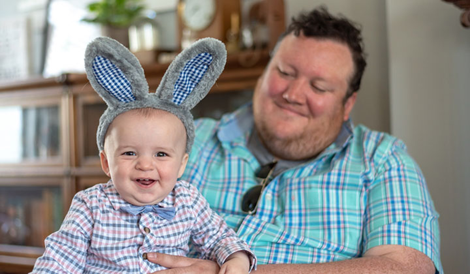 Smiling baby wearing bunny ears sitting on his dad's lap