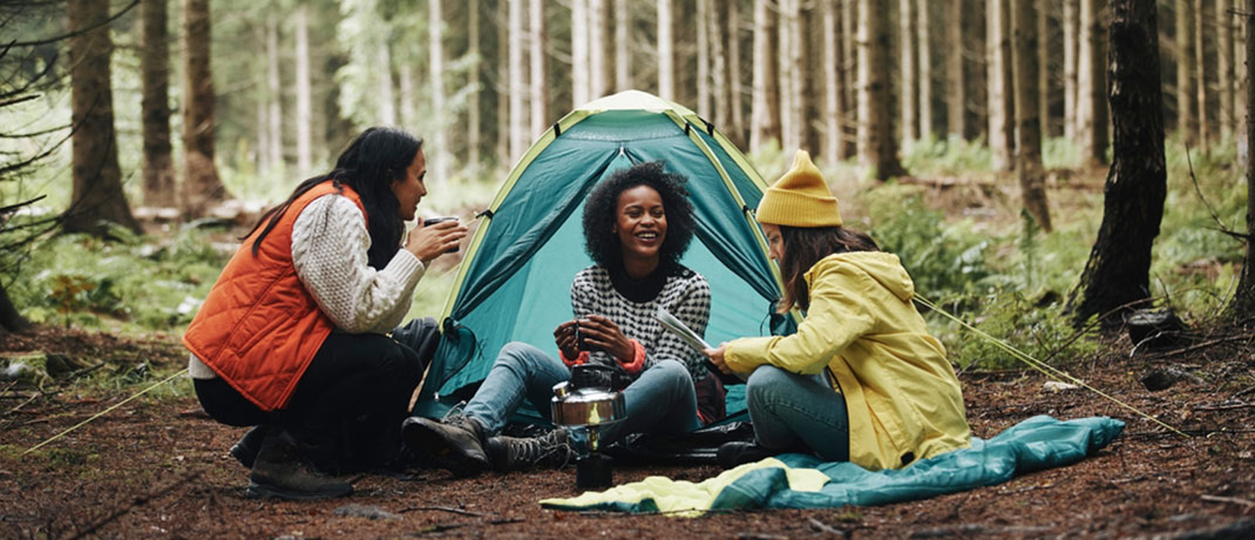 Three smiling young women camping by a tent