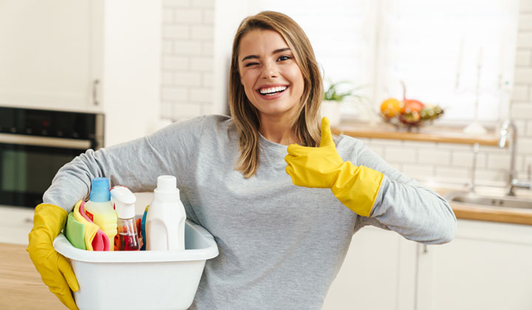 Smiling young woman holding bucket of cleaning supplies
