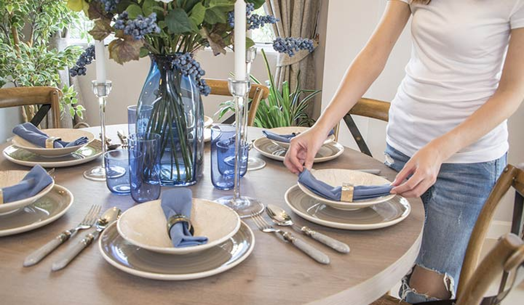 Woman setting a table with white dishes and blue accessories