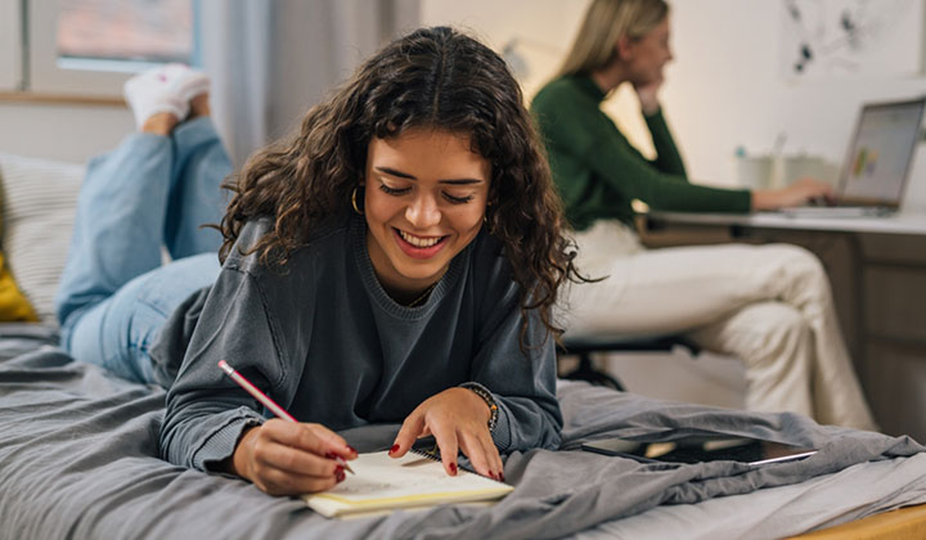 Smiling college student doing homework on her bed