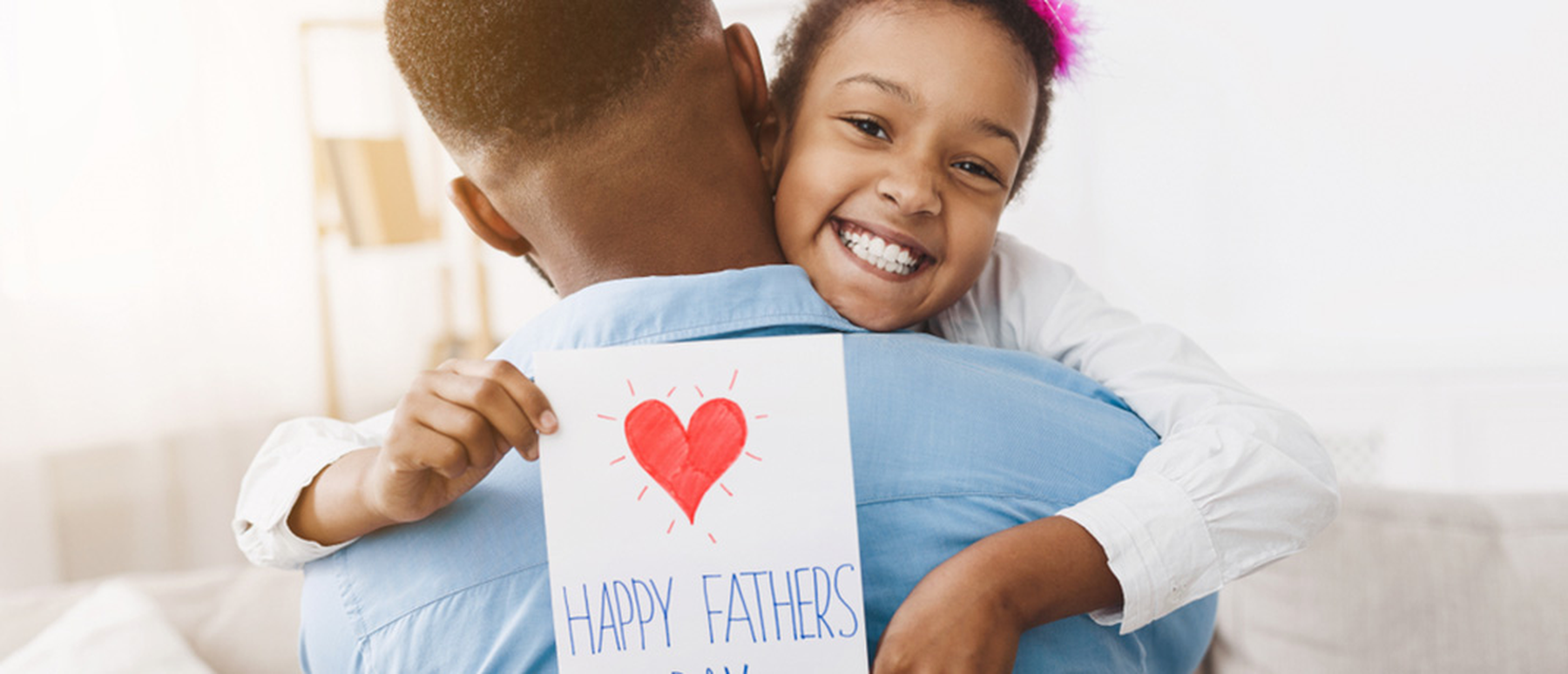 Young smiling girl hugging dad holding a happy Father's Day card