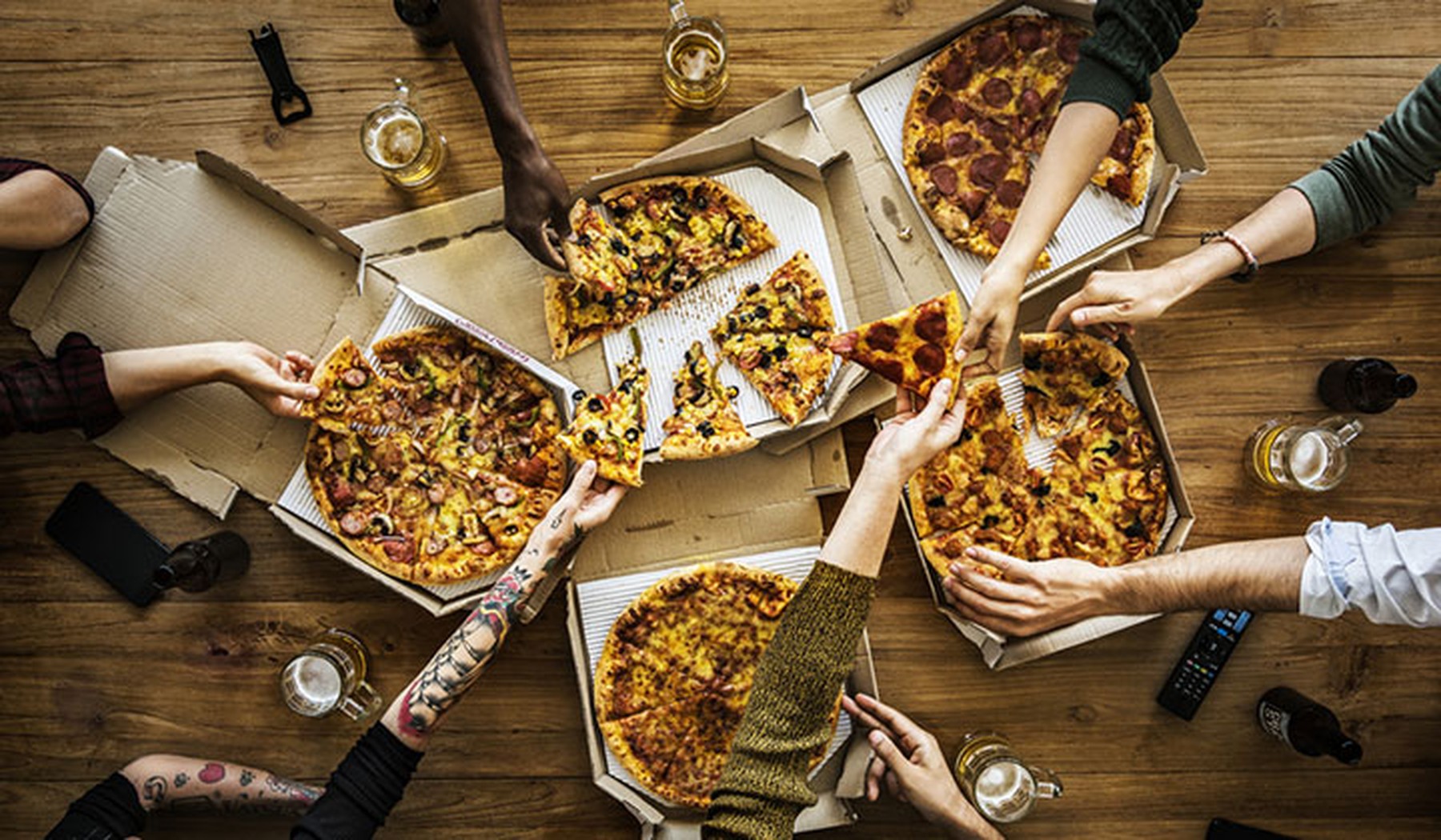 Group of people reaching for pizza out of many boxes