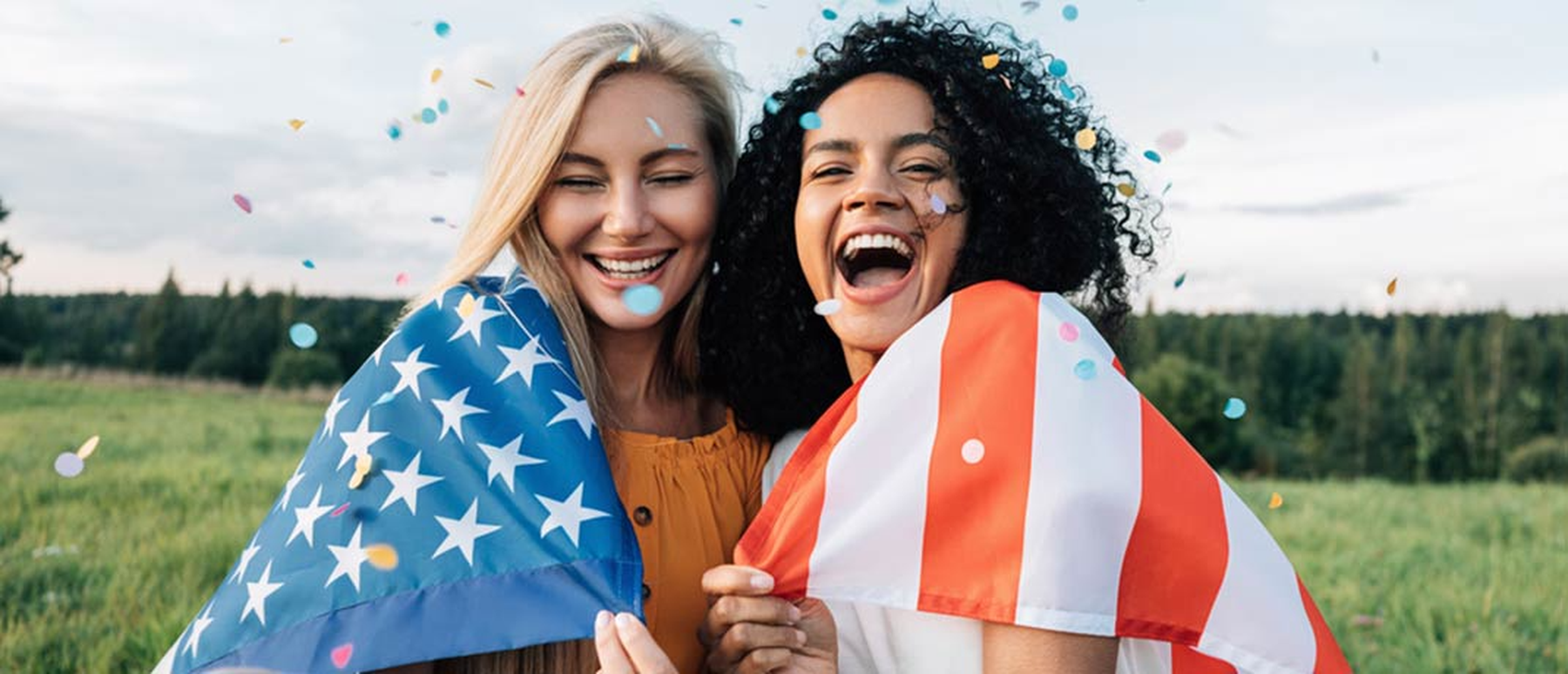 Young smiling women wrapped in an American flag throwing confetti
