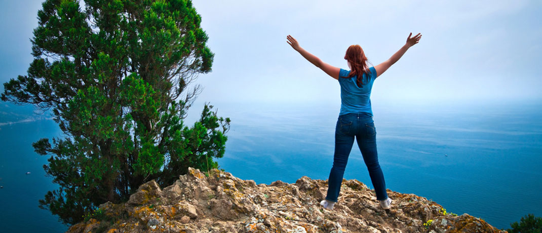 Woman standing on a cliff above the sea with her arms raised