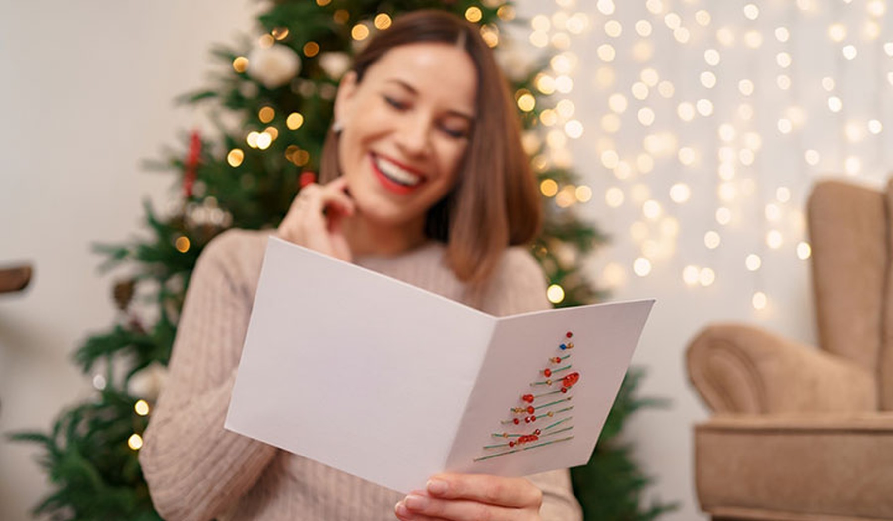 Smiling woman reading card in front of Christmas tree
