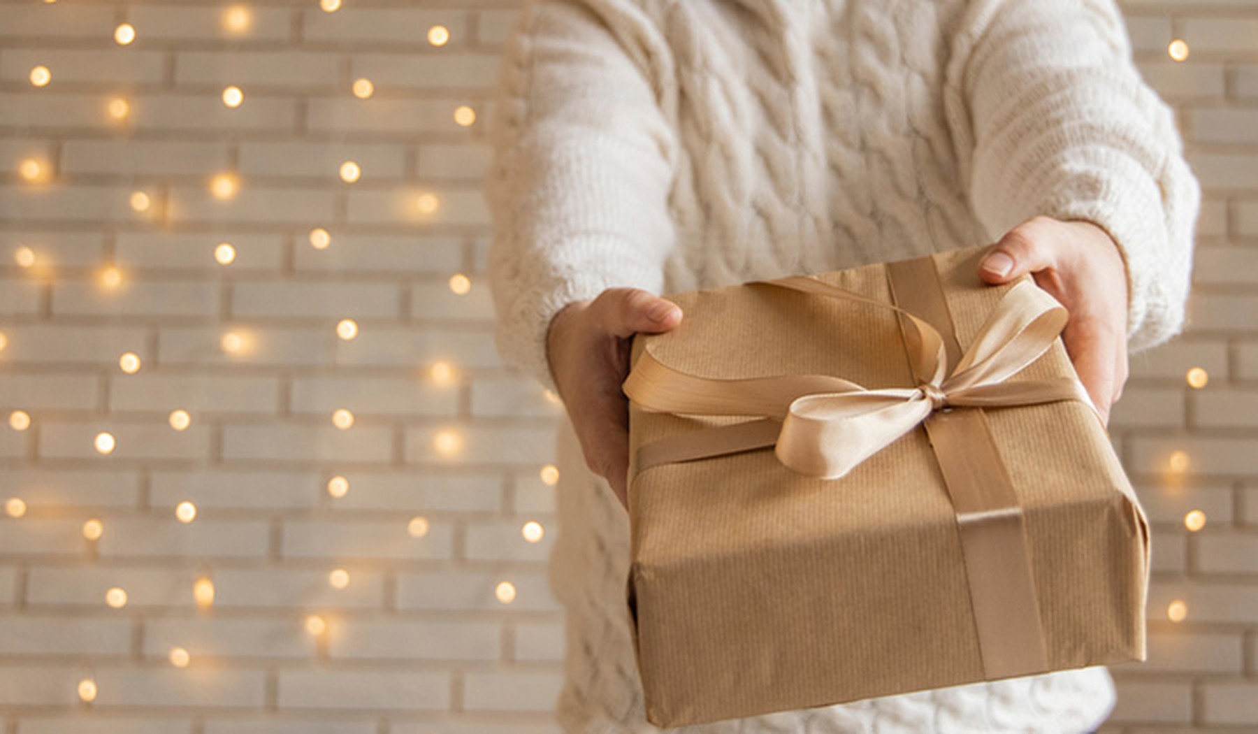 Person holding wrapped holiday gift in front of white lights