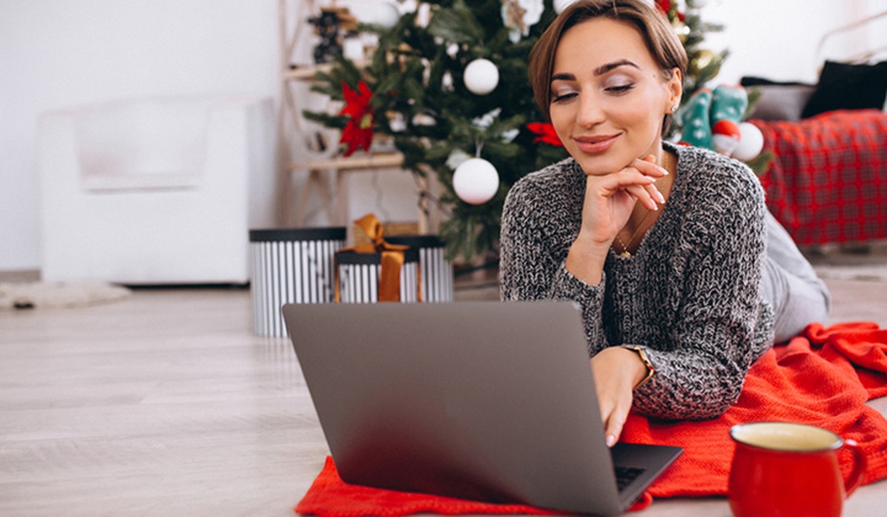 Woman in front of Christmas tree looking at her laptop