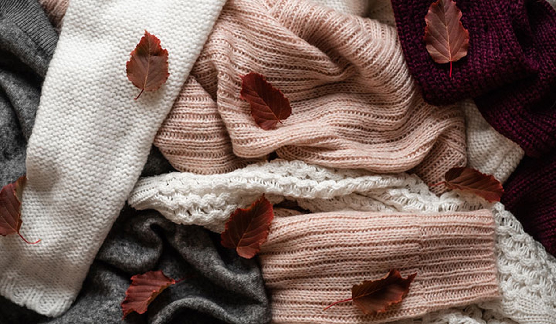 Folded sweaters with fall leaves scattered on top