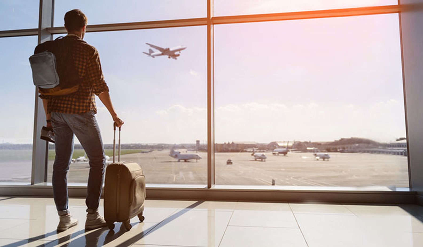 Man with rolling luggage staring at plane taking off