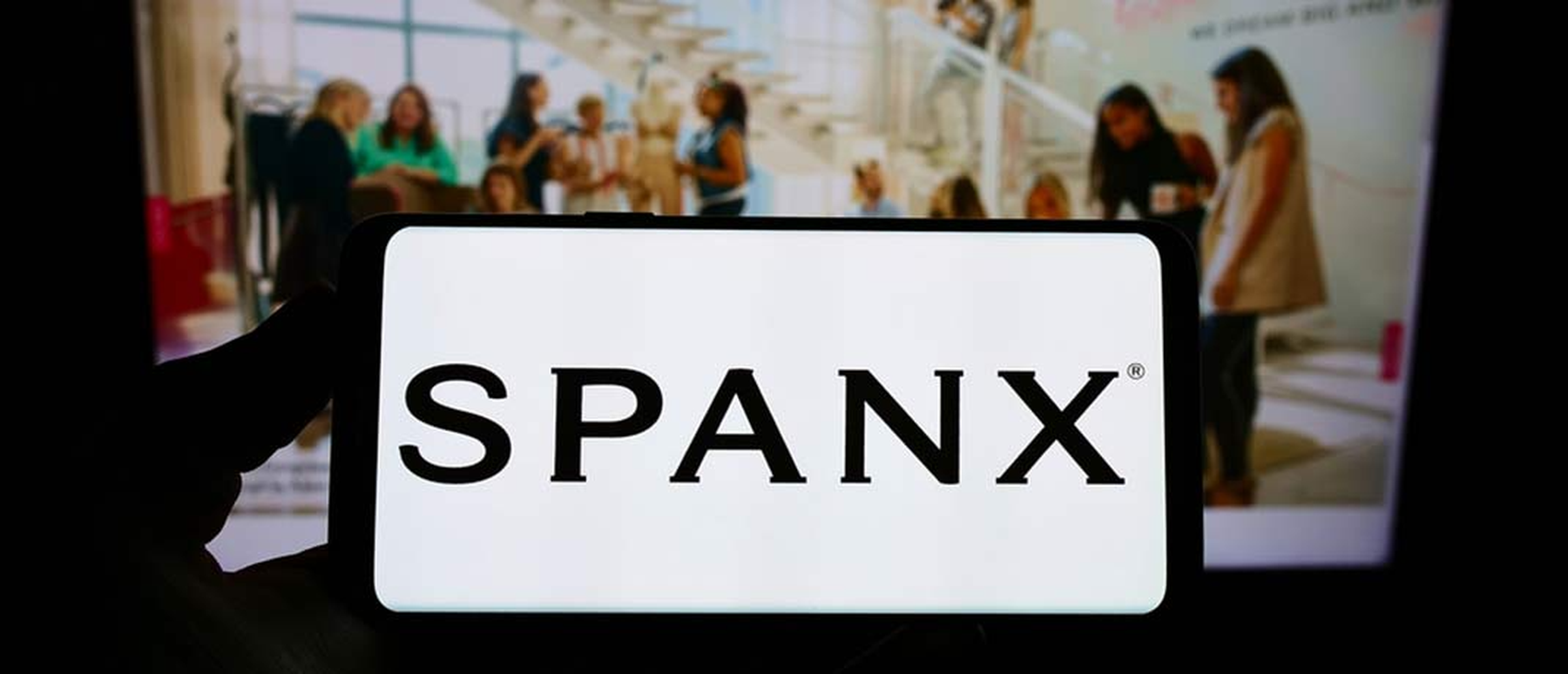 Spanx name on phone with Spanx homepage on a computer in the background