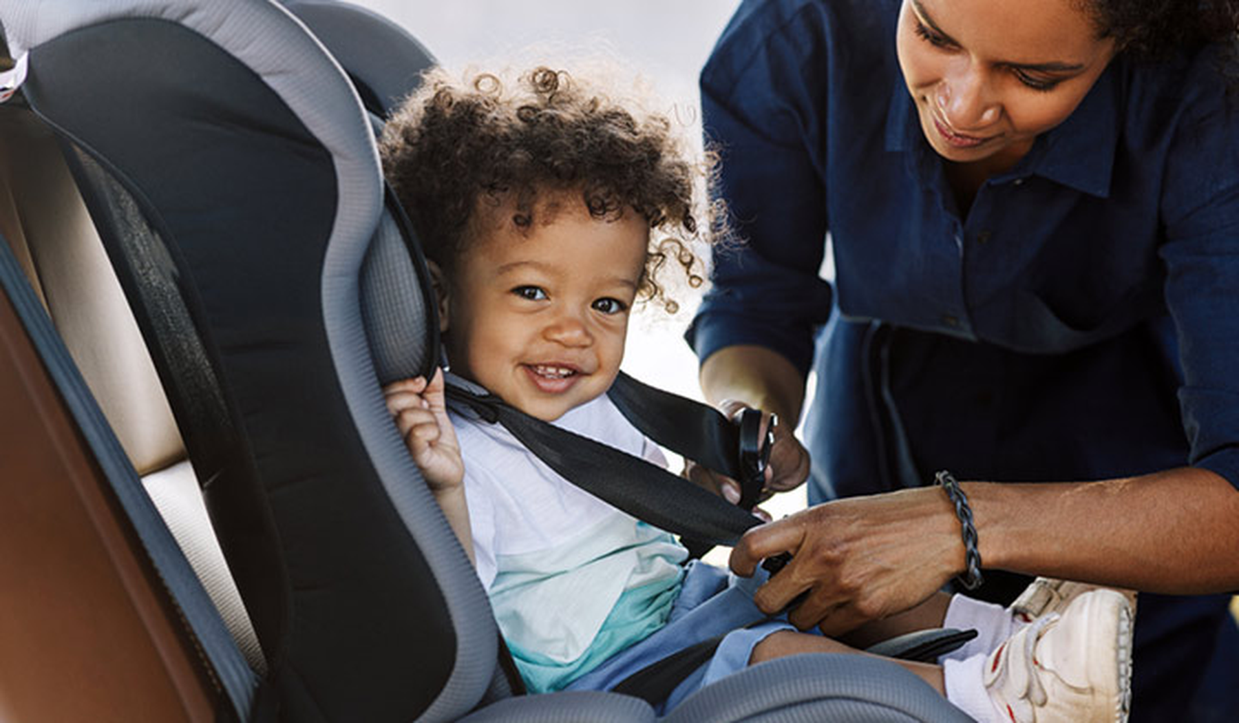 Toddler getting strapped into a car seat by his mom