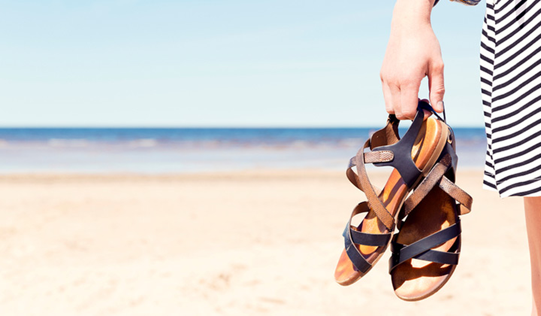 Woman holding sandals on a beach