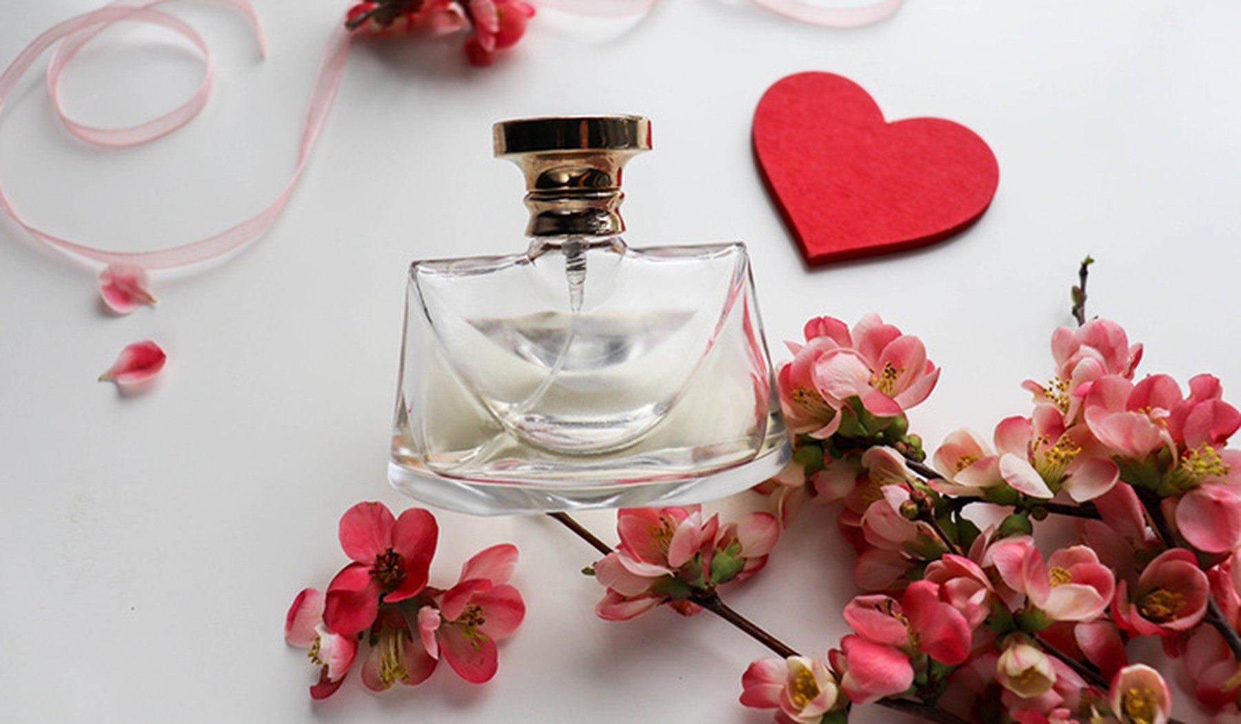 Perfume bottle in front of a red paper heart and pink flowers