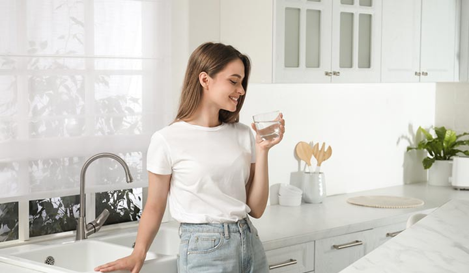 Smiling young woman holding a glass of water in the kitchen