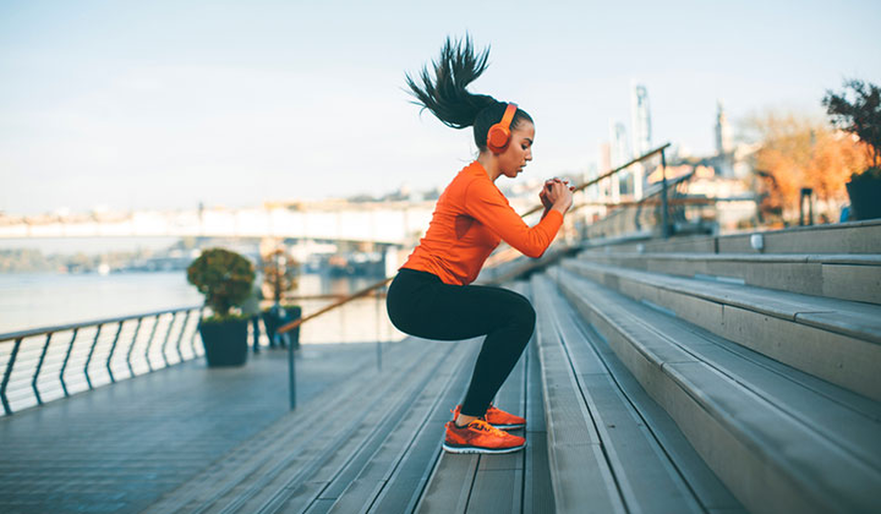 Young woman in an orange top exercising by jumping up stairs