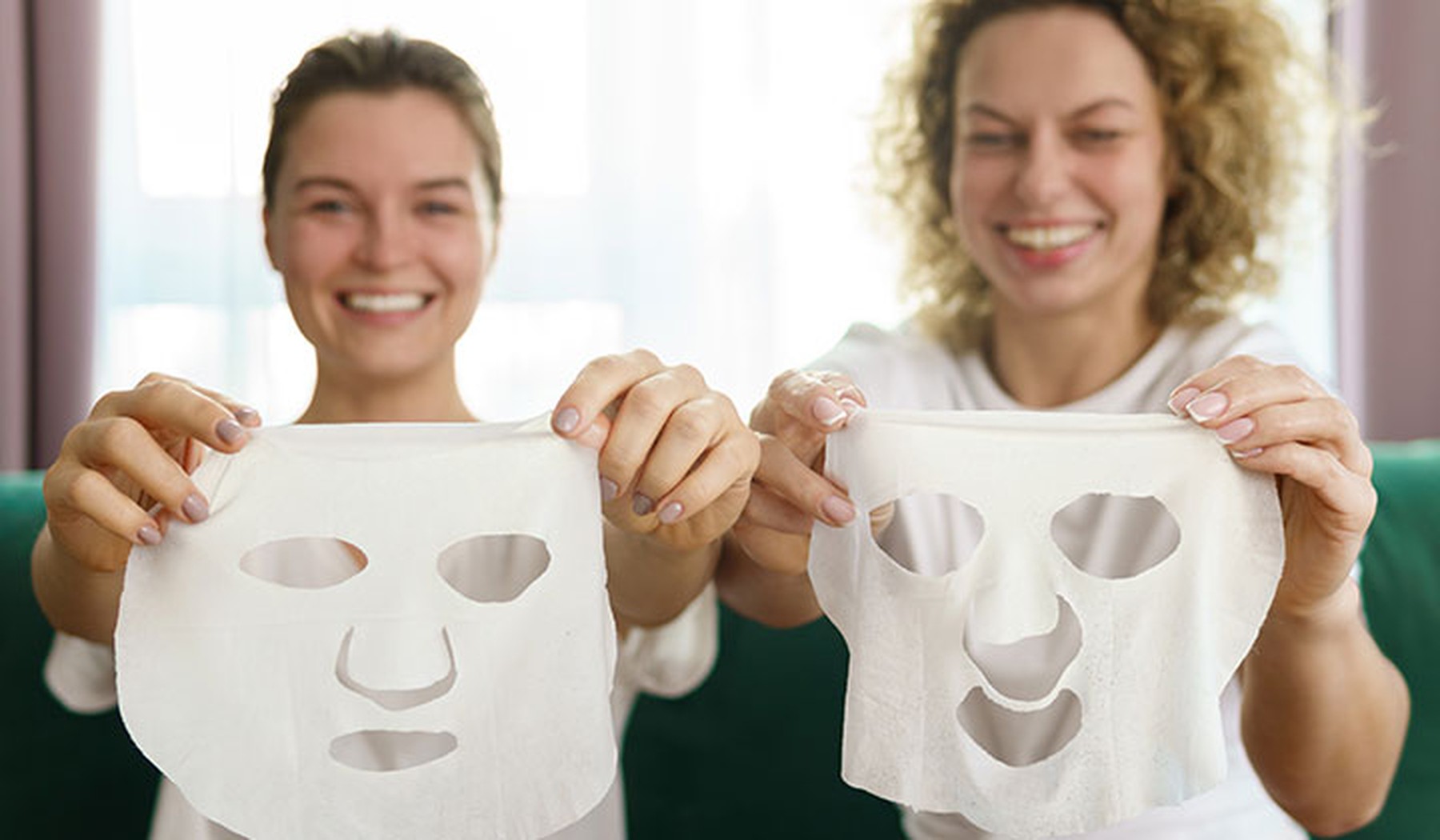 Two smiling young women holding up face masks
