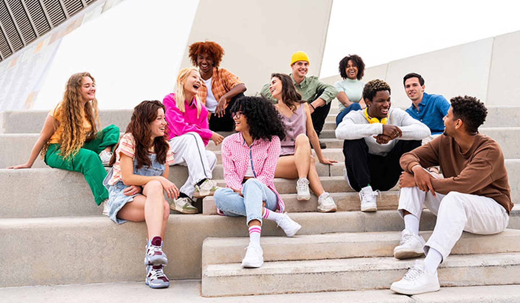 Group of happy teens sitting on stairs wearing casual clothes and sneakers 