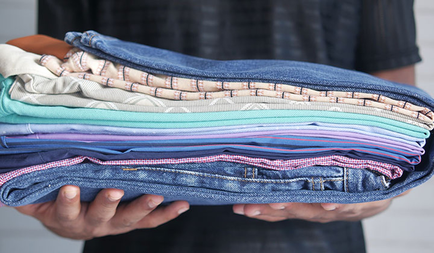 Man holding a pile of jeans and tees